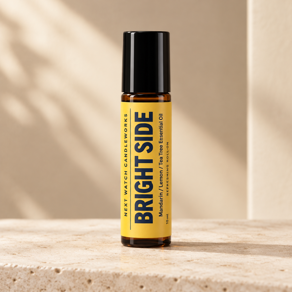 A small amber glass roll-on bottle of Bright Side Mandarin / Lemon / Tea Tree Essential Oil by Next Watch Candleworks, featuring a bright yellow label and black cap, set on a textured stone surface with warm, sunlit shadows.