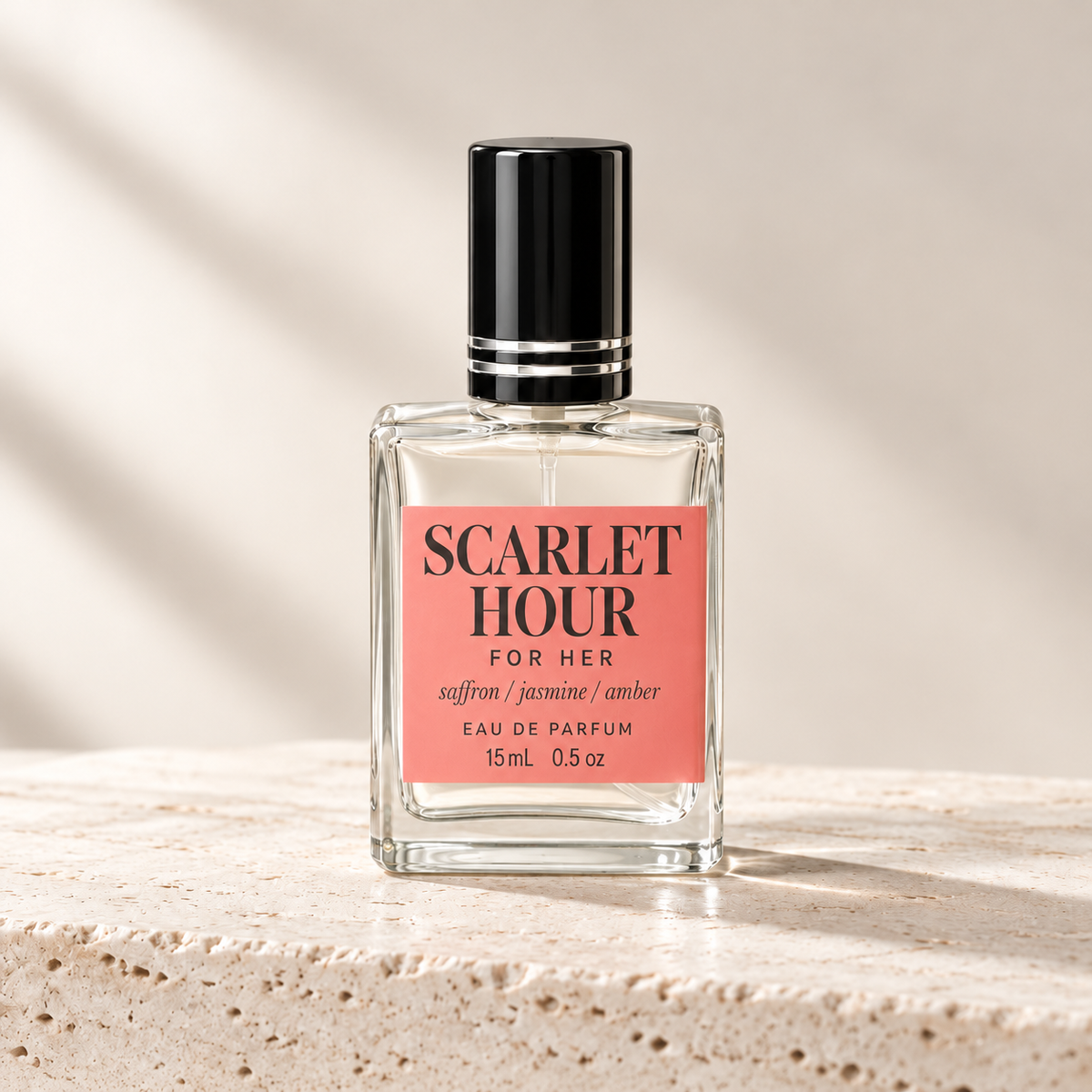 Scarlet Hour For Her Eau de Parfum in a clear glass bottle with a black cap and a coral pink label, set on a textured beige stone surface with soft diagonal shadows.